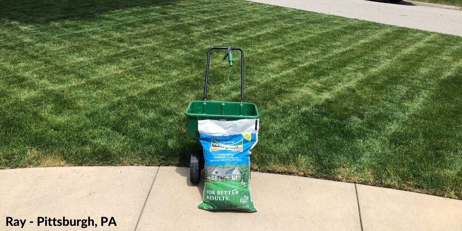 A bag of Milorganite fertilizer and spreader in the lawn.