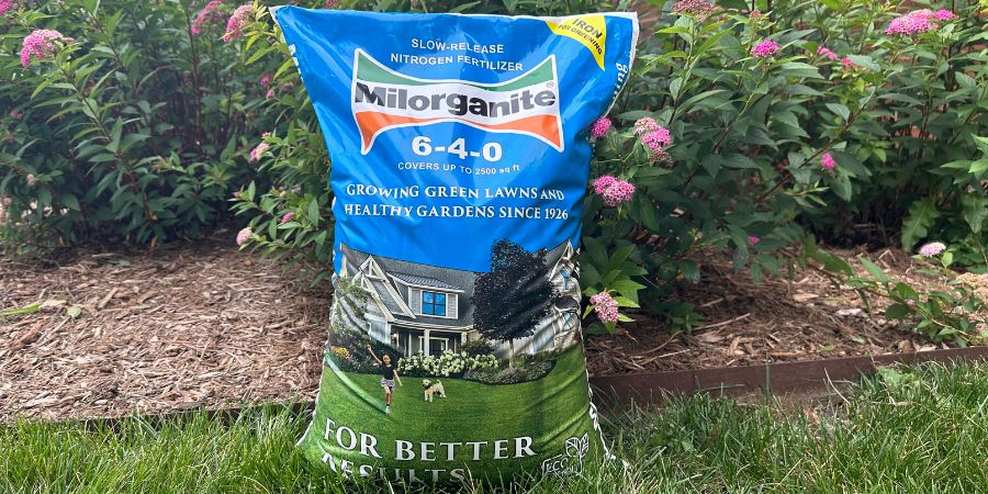 A bag of Milorganite fertilizer in the lawn with pink flowers
